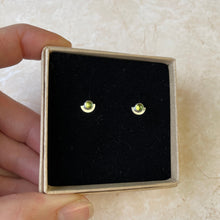 Load image into Gallery viewer, A pair of small peridot stud earrings set in gold, presented in a black box with gold stamping, the earrings are likely sterling silver