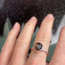 Load image into Gallery viewer, Hand wearing a ring with a smokey quartz gemstone against a blurred background
